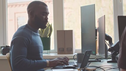 African American male software engineer with colleague working on desktop computers in modern office
