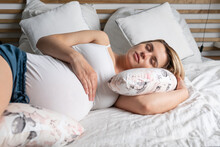 Pregnant Woman Restful Sleeping In Bed Using Special Pillow For Belly Support