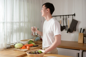 Wall Mural - An Asian young man drinking fresh water in kitchen at home , healthy lifestyle concept