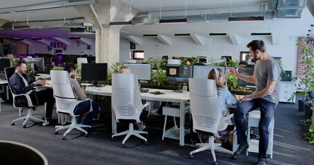 Rear of people developers sitting at computers and working. Back view on support office employees. Man coming and helping in IT work to woman colleague. Male and female talking and discussing.