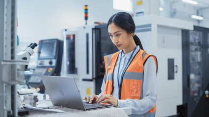Fototapete - Portrait of an Asian Female Engineer in Orange Safety Vest Working on Laptop Computer at Electronic Manufacturing Factory. Technician Working on Daily Tasks and Inserting Analytic Science Data.