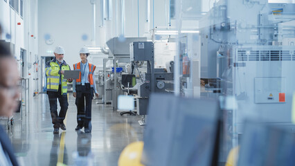 Fototapete - Two Professional Heavy Industry Employees Wearing Hard Hats at Factory. Checking and Discussing Industrial Machine Part, Working on Laptop Computer. Asian Engineer and Middle Aged Technician at Work.