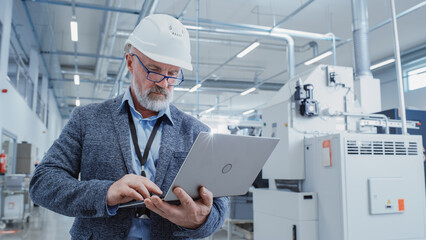 Aufkleber - Portrait of a Bearded Middle Aged Chief Engineer Walking in a Factory Facility, Wearing Casual Suit and a White Hard Hat. Heavy Industry Specialist Working on Laptop Computer.