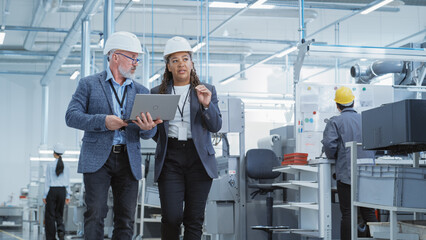 Poster - Two Heavy Industry Engineers in Hard Hats Walking with Laptop Computer and Talking in a Factory. Footage of Two Manufacturing Employees at Work in Production Facility.