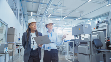 Aufkleber - Two Professional Heavy Industry Employees in Hard Hats at Factory. Checking and Discussing Industrial Facility, Working on Laptop Computer. African American Engineer and Asian Technician at Work.
