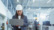 © Gorodenkoff - Portrait of an African Female Engineer in Hard Hat Standing and Using Laptop Computer at Electronic Manufacturing Factory. Technician Working on Analytical Data Collected from Modern Equipment.