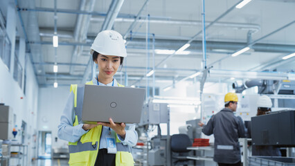 Fototapete - A Happy and Smiling Asian Female Engineer in White Hard Hat Standing with Laptop Computer at Electronic Manufacturing Factory. Successful Employee Focusing on PC Screen