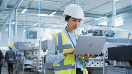 Fototapete - A Focused and Professional Asian Female Engineer in White Hard Hat Standing with Laptop Computer at Electronic Manufacturing Factory. Successful Employee Working on Daily Tasks