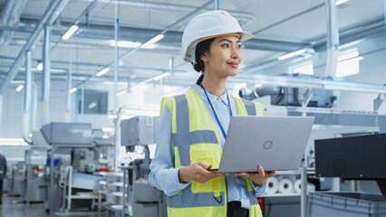 Fototapete - A Happy and Smiling Asian Female Engineer in White Hard Hat Standing with Laptop Computer at Electronic Manufacturing Factory. Successful Employee Focusing on PC Screen