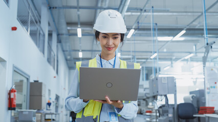 Fototapete - A Happy and Smiling Asian Female Engineer in White Hard Hat Standing with Laptop Computer at Electronic Manufacturing Factory. Successful Employee Focusing on PC Screen