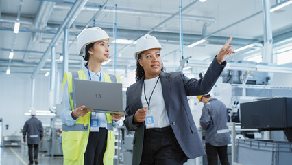 portrait of two female employees in hard hats at factory. discussing job assignments at industrial m