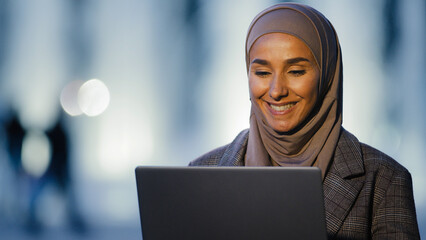 Portrait ethnic islamic muslim business woman girl international student speaks video chat conference using laptop talking in web camera sitting in evening night on street in city remote conversation