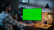 © Gorodenkoff - Young Handsome Man Working from Home on Desktop Computer with Green Screen Mock Up Display. Creative Male Checking Social Media, Browsing Internet. Loft Living Room in the Evening