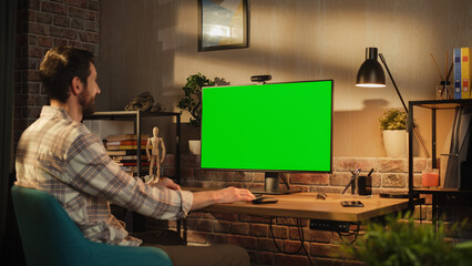 Aufkleber - Young Professional Creative Specialist Works on His Personal Desktop Computer with Big Monitor with Green Screen Mock Up Display. He Works in a Cozy Office Loft in the Evening.