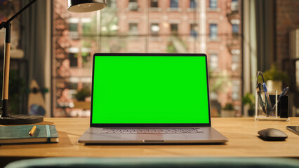 Poster - Laptop Computer Display with Mock Up Green Screen Standing on a Wooden Desk in Living Room. Chroma Key Monitor at Home or Creative Loft Office With Notepad, Mouse and Pencil