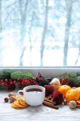 Festive Christmas decor on windowsill. tangerines, dried orange slices, nuts, cinnamon, coffee or tea cup on table. Christmas holiday. cozy winter season, cold snowy weather