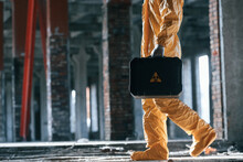 The Case With Biohazard Sign On It. Man Dressed In Chemical Protection Suit In The Ruins Of The Post Apocalyptic Building