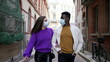 © Marco - Interracial couple wearing covid-19 face mask walking outside in street