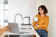 © Prostock-studio - Young Smiling Arab Woman Using Laptop And Drinking Coffee In Kitchen