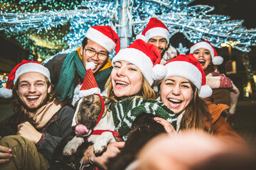 Happy friends wearing santa claus hat celebrating Christmas night together on city street 