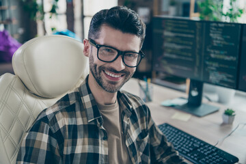 Portrait of cheerful hacker guy sit leather chair toothy smile operate pc server open space workstation indoors