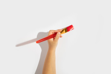 Child's hand holds a paintbrush on a white background. Top view, flat lay