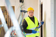 © JackF - Repair man in yellow vest and helmet with level in hands standing in apartment and looking at camera.