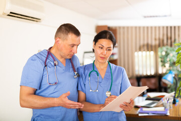 Wall Mural - Two professional doctors checking the patient papers in a doctor office in clinic