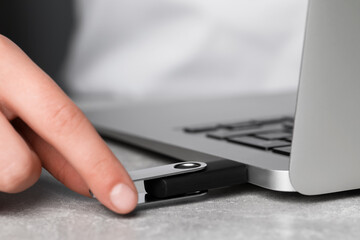 Woman attaching usb flash drive into laptop at light grey table, closeup