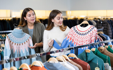 Wall Mural - Positive young women friends choosing winter sweater in the fashion store