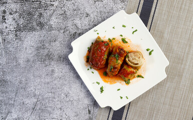 Wall Mural - Stuffed cabbage rolls with meat, rice and tomato sauce on a white square  plate on a dark background. Top view, flat lay