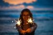 Young woman holding sparkler celebrating new years eve on the beach