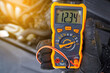 Checking car battery voltage. Mechanic check up car electric system with multimeter in cold winter conditions. Man with voltmeter measuring voltage level in car battery. Testing battery health