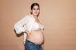 Confident Hispanic pregnant woman standing in studio with hand on waist