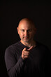 © Aleksandr - Vertical photo of a bald man in a black jacket, who points his index finger at the camera and looks there, on a black background.