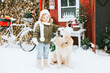 © klavdiyav - cute little girl in knitted sweater and hat having fun with first snow and cute pet dog labrador at porch of country house, concept of winter spirit and Christmas
