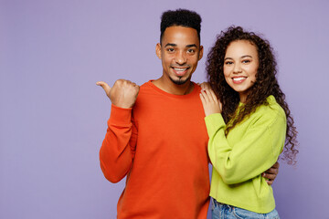 Young smiling happy couple two friend family man woman of African American ethnicity wear casual clothes point thumb finger aside on area hug together isolated on pastel plain light purple background