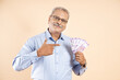 © GAJENDRRA BHATI  - Happy senior Indian man holding money of 100 rupee notes isolated on beige background, Asian mature male with lot of cash in hand.