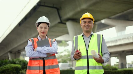 Wall Mural - Confident Male and Female Engineer or architect looking camera with safety helmet in construction site. Two Supervisor engineers working at construction project. Civil engineering concept.