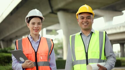 Wall Mural - Confident Male and Female Engineer or architect looking camera with safety helmet in construction site. Two Supervisor engineers working at construction project. Civil engineering concept.