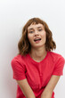© Tatiana - vertical photo of a beautiful, sweet woman standing on a light background in a red T-shirt and smiling pleasantly at the camera