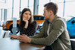 © makedonski2015 - A young couple is sitting at a table in a dealership and waiting for a sales manager. Buying a new family car