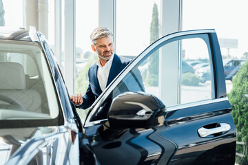Mature handsome stylish man in car sales center. Mature man choosing new automobile.