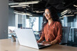© Liubomir - Cheerful and successful indian woman programmer at work inside modern office, tech support worker with laptop typing on keyboard smiling.