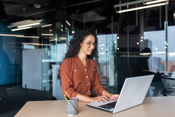 Cheerful and successful indian woman programmer at work inside modern office, tech support worker with laptop typing on keyboard smiling.
