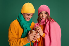Portrait Of Young Man And Woman In Bright Knitted Hat And Scarf Posing Isolated Over Green Background. Happiness And Merry