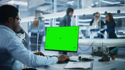 Software Developer Working on Computer with Green Screen Mock Up Display. Scientific Lab, Engineering Research Center with Specialists Working on Mobile Robot Development in the Background.