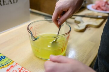 Close-up shot of a male hand stirring the yellow liquid with a spoon in a measuring cup