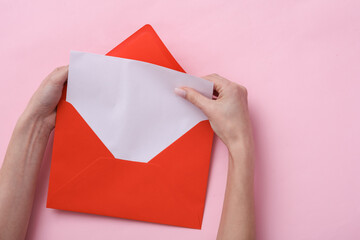 Poster - Female hands hold a red envelope with an empty white letter on pink background