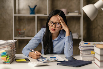 Asian female accountant stressed overtime with loose paperwork and holding hands on head Woman worried and stressed with hard work in the office